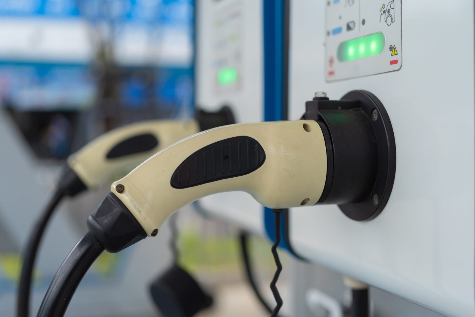Conector de estação de recarga plugado em veículo elétrico, com indicadores luminosos de carregamento.